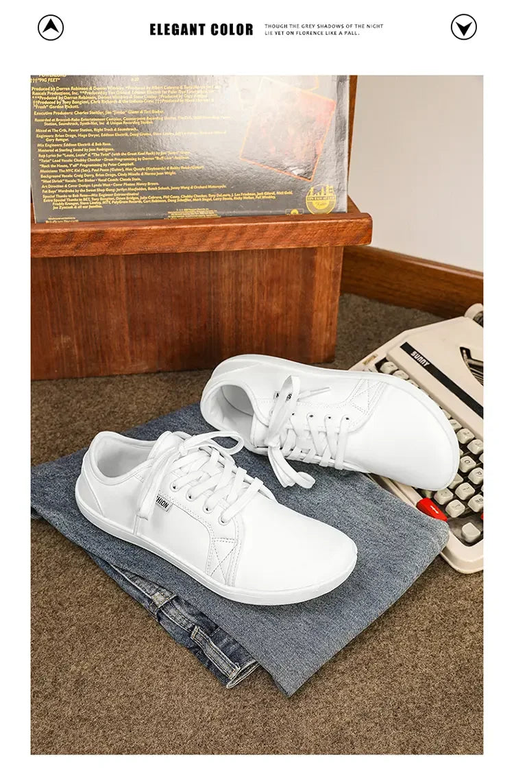 Wide Version barefoot shoes white, lightweight casual sneakers atop folded jeans beside a vintage typewriter