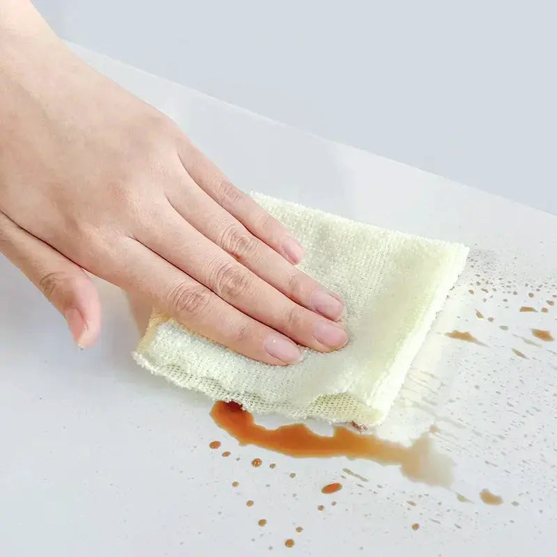 Imitation marble self-adhesive tile wallpaper being wiped by hand on a white surface with a brown spill