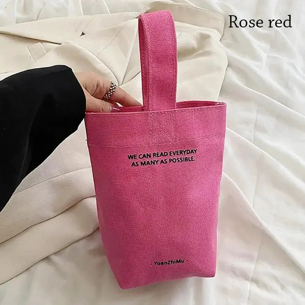 Casual canvas handbag in pink with short handles; tote-style bag with bold printed text.