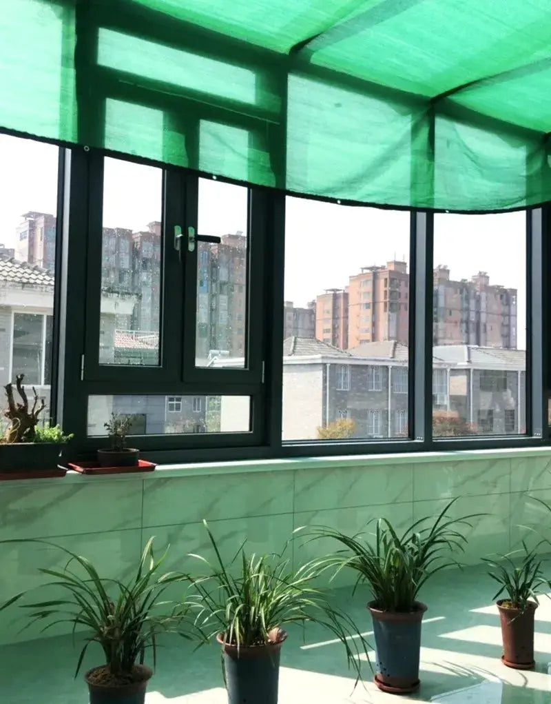 HDPE sun shade net in green over balcony; four potted plants line the railing.