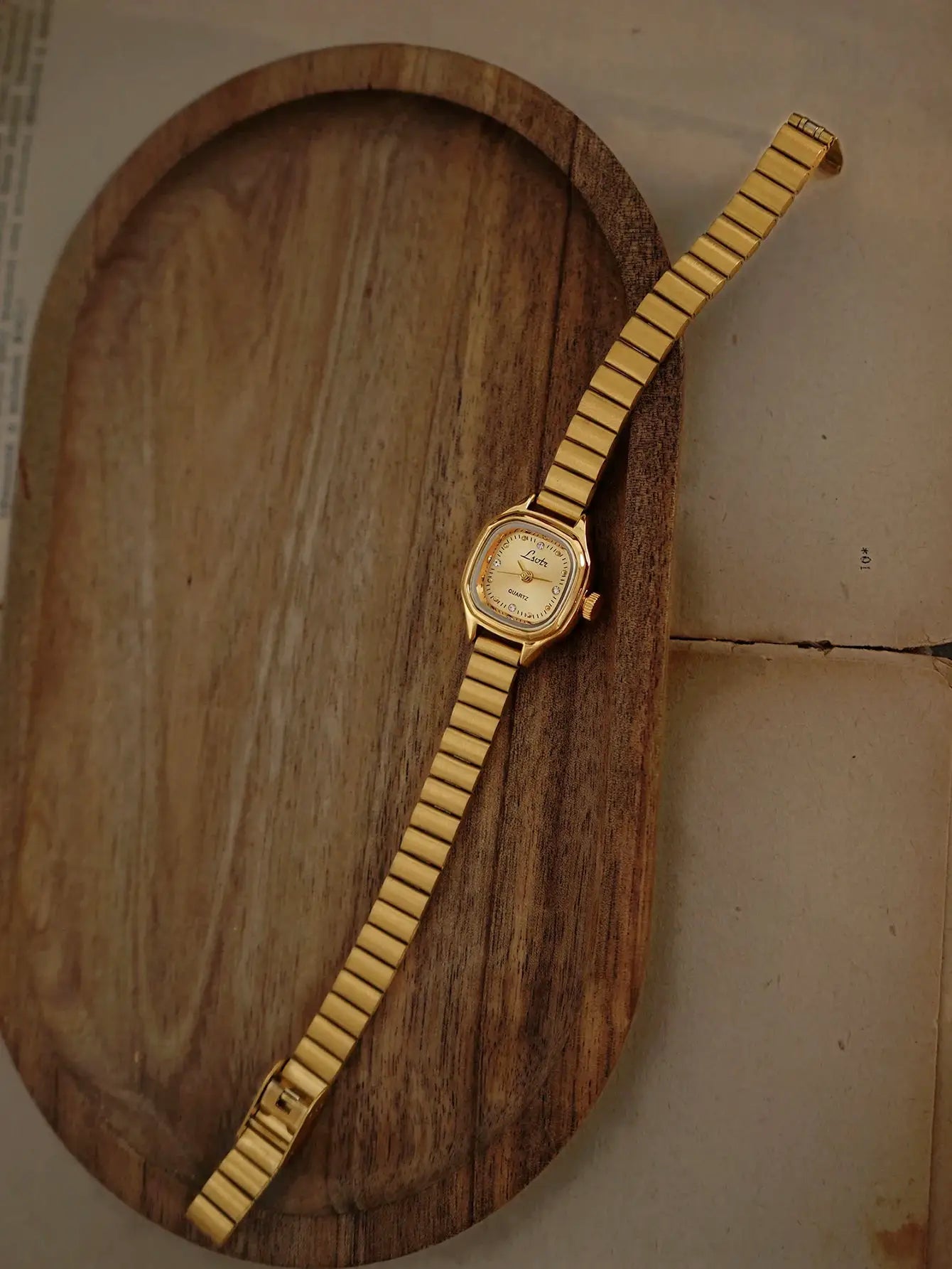 Gold-tone square-faced women's watch with a stainless steel bracelet resting on a wooden surface