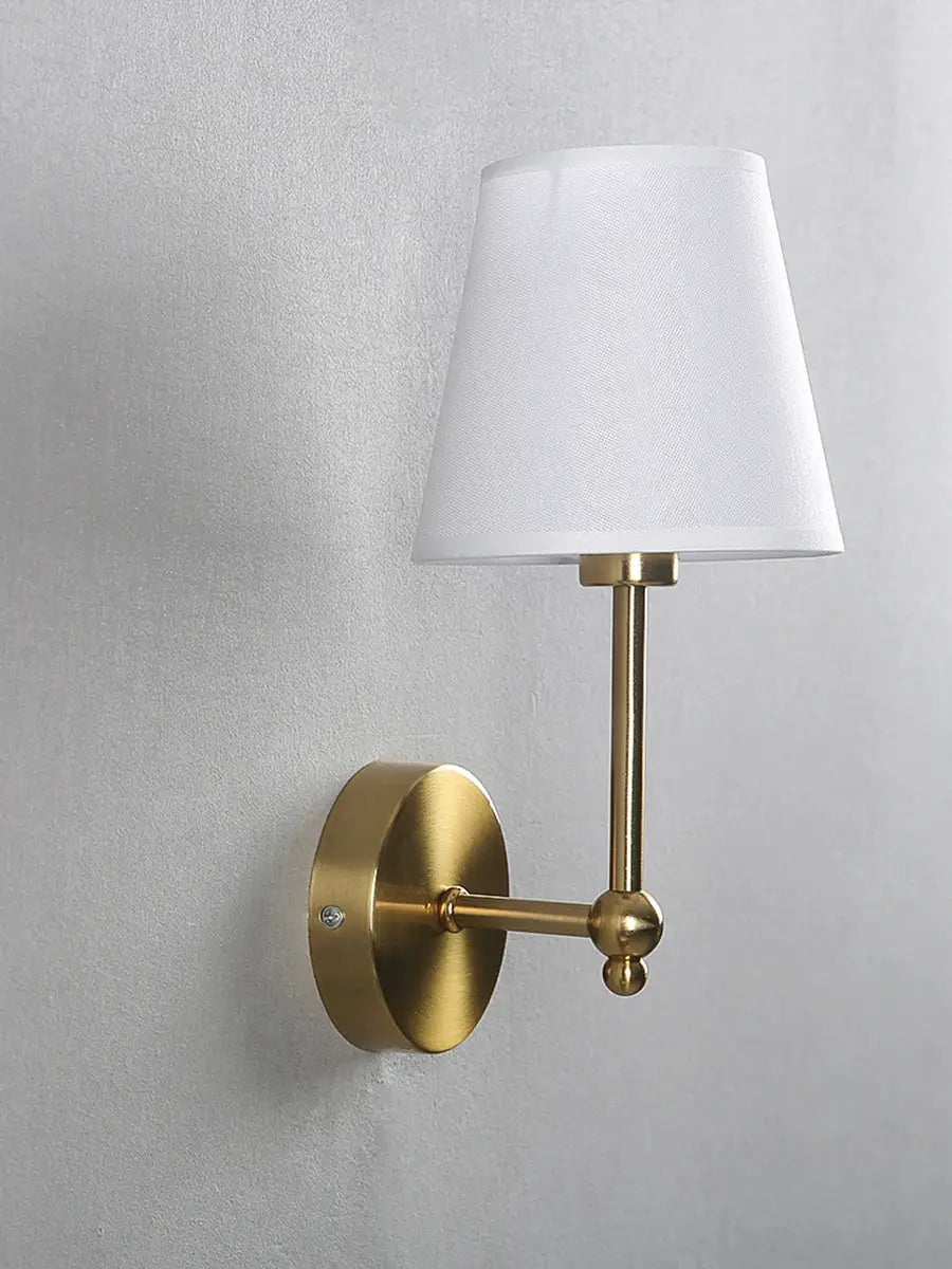 Wall sconce in brass finish with white fabric shade; ideal bedside lamp.