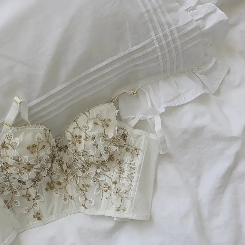 Cream three-dimensional embroidered bra with gold floral lace and white straps on a white bed