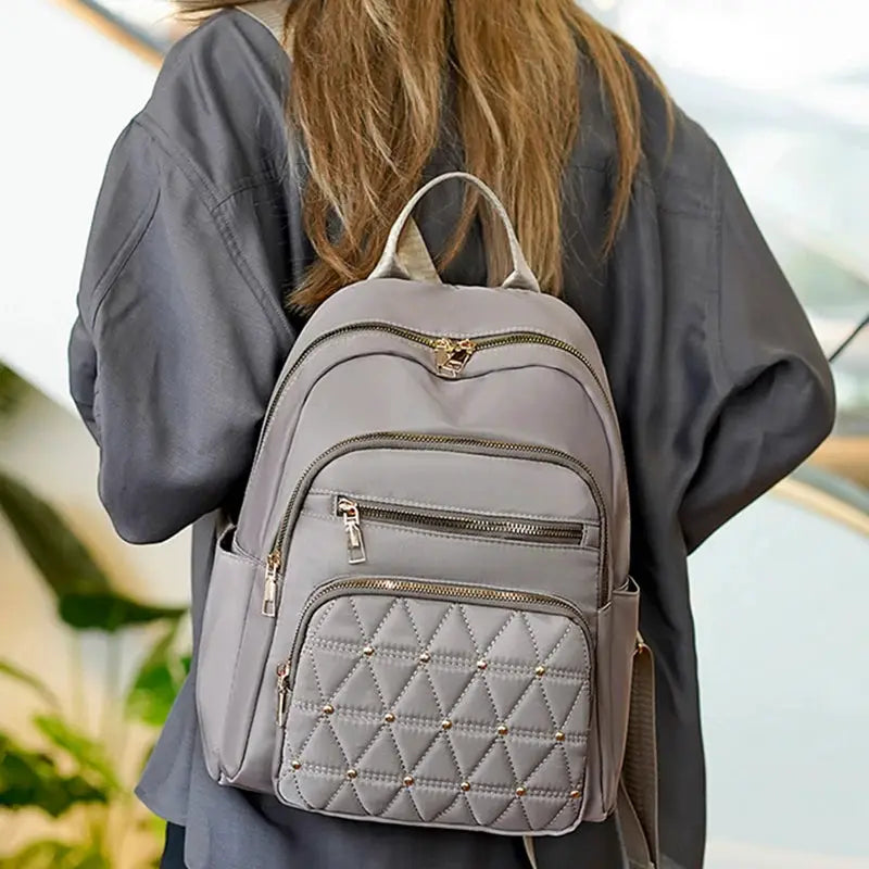 Travel backpack in gray with quilted front pocket and multiple zip compartments, gold-tone hardware.