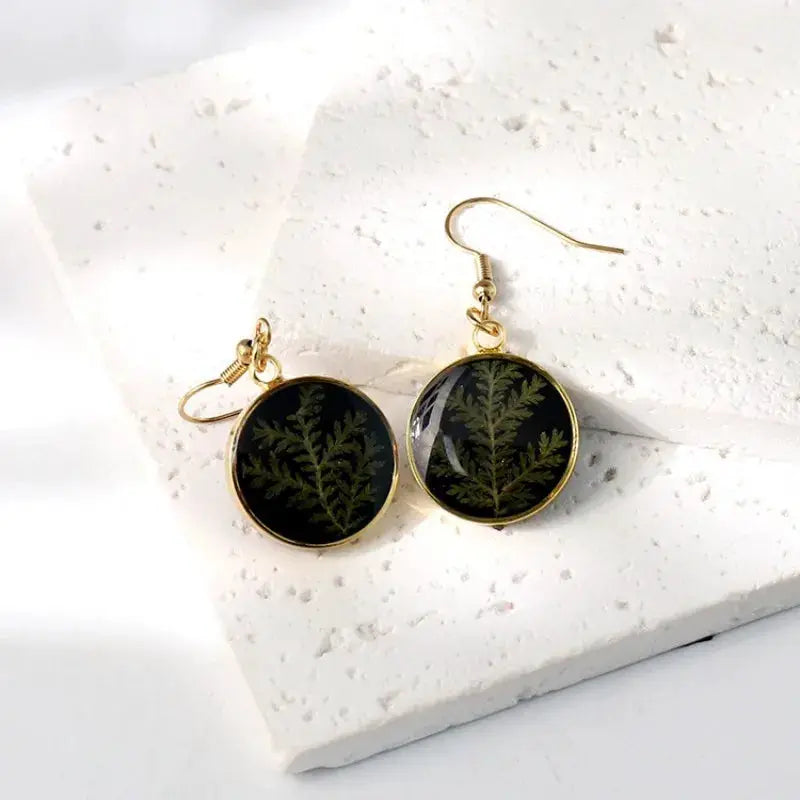 Earrings by Simples Market: round gold-tone frames with pressed fern leaf in black epoxy resin