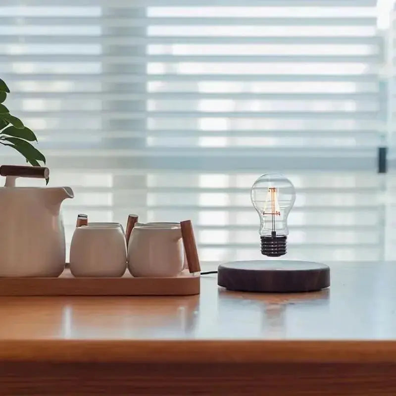Magnetic levitation lamp with a floating glass LED bulb on a dark round base beside a tea set on a wooden desk