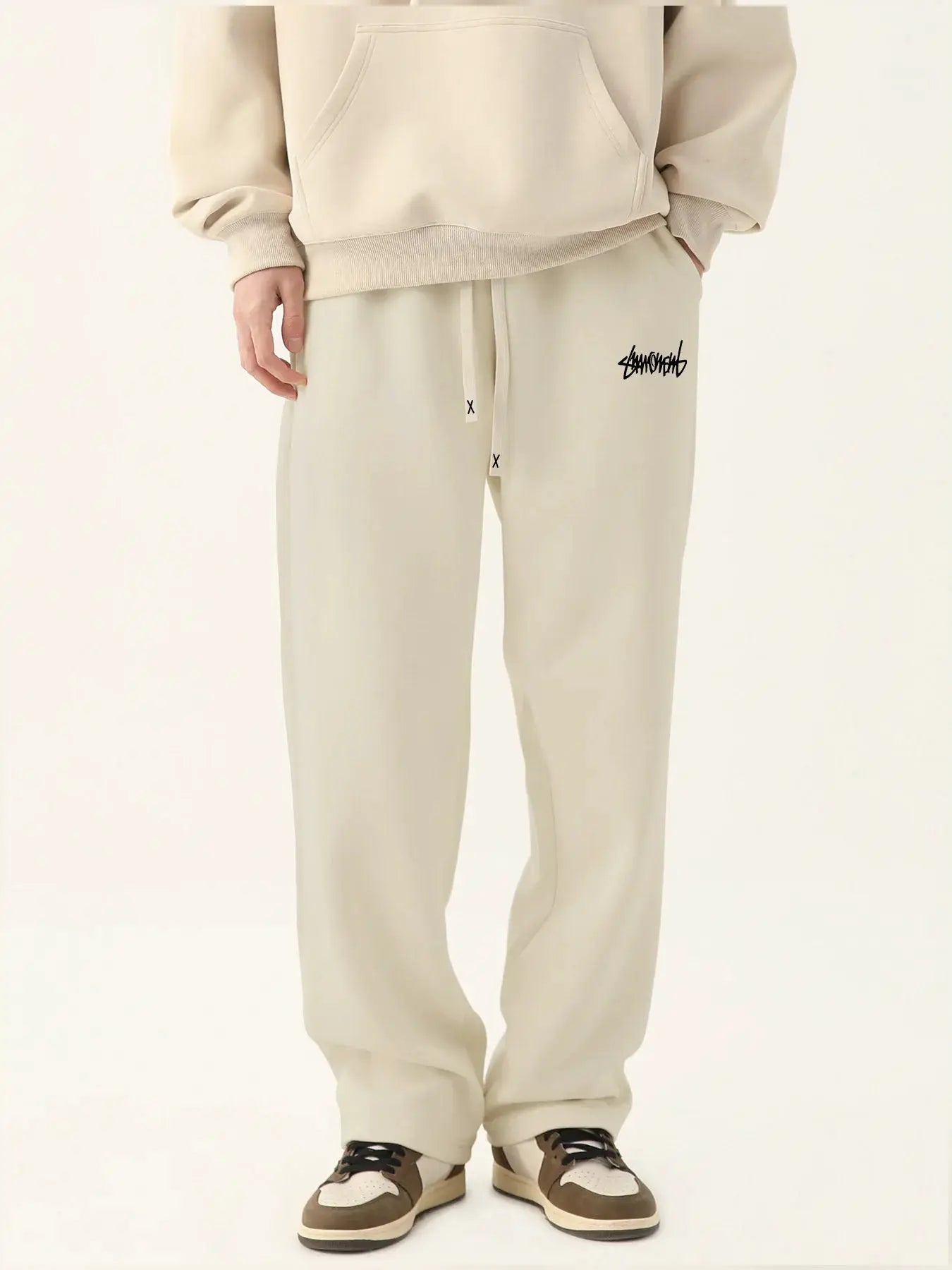 Men's beige baggy jogger pants in neutral breathable fabric with drawstring waist and logo graphic on thigh