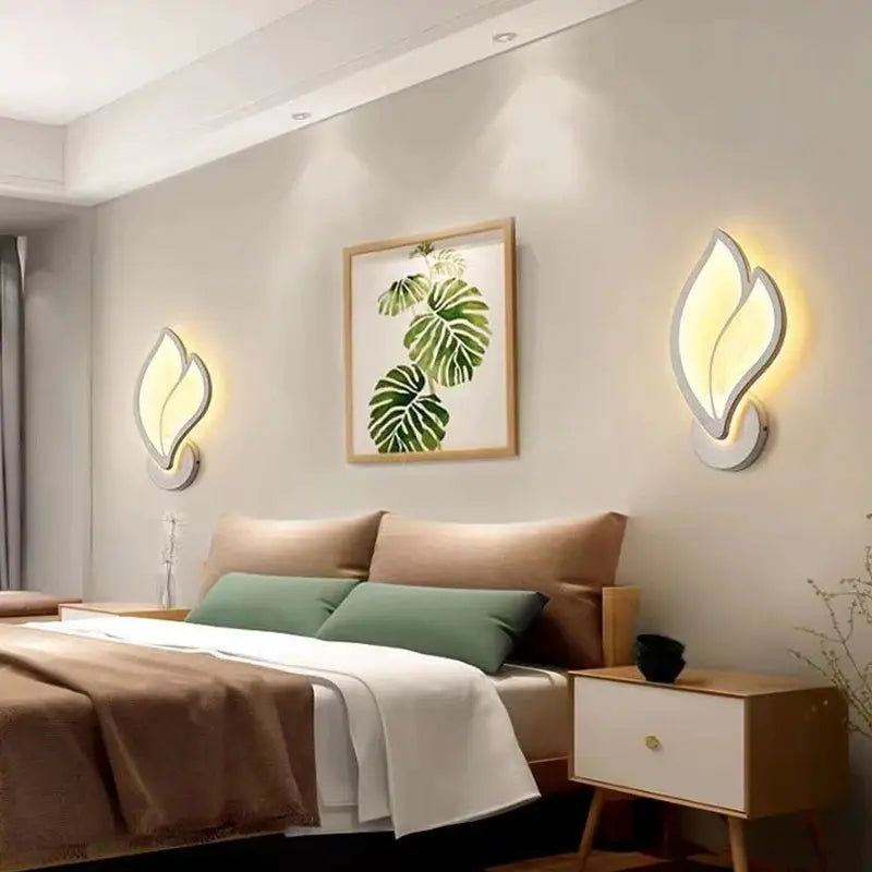 Two modern LED wall lamps with warm yellow glow flanking a framed plant artwork above a bed