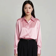 Pink satin blouse with collar and long sleeves, paired with black high-waisted pants.