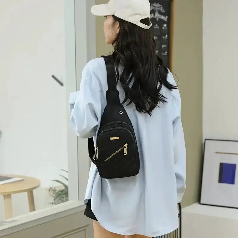 Backpack in black fabric with gold zippers, worn by a model in a light blue shirt and white cap with adjustable straps