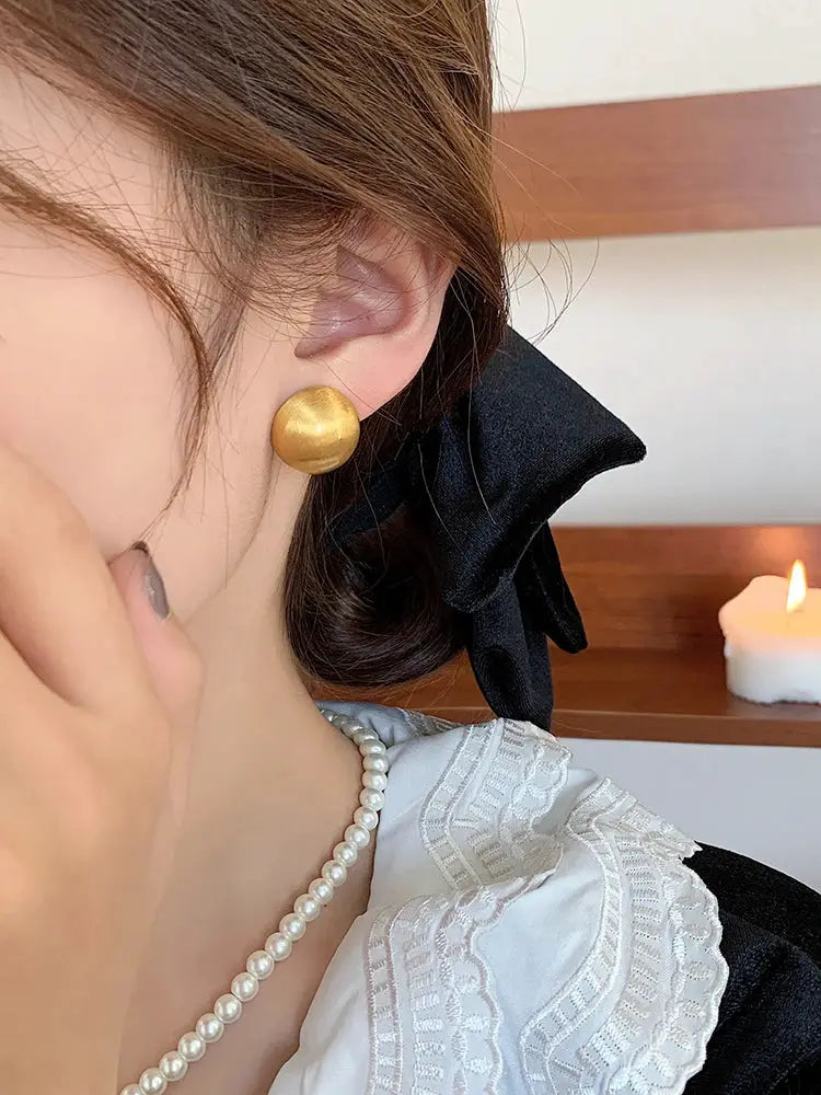 Semicircle earrings by Simples Market in brushed gold metal worn on the ear, with a pearl necklace and lace blouse
