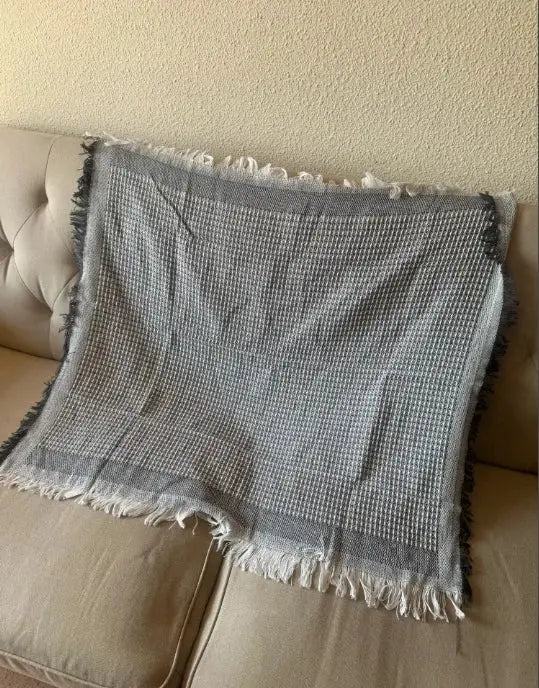 Gray woven sofa throw blanket with fringe on a beige couch