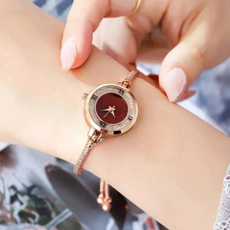 Women's rose-gold bracelet wristwatch with crystal-studded bezel and small red dial.