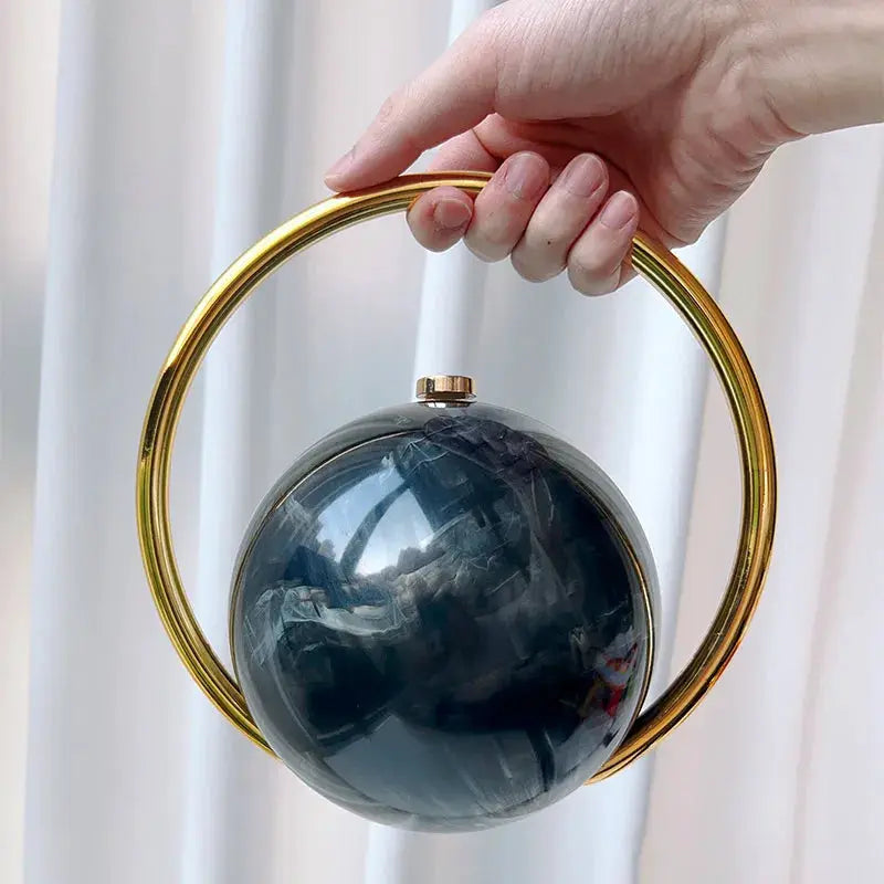 Luxury acrylic evening clutch with gold circular ball-handle hoop and dark marbled blue-green spherical body