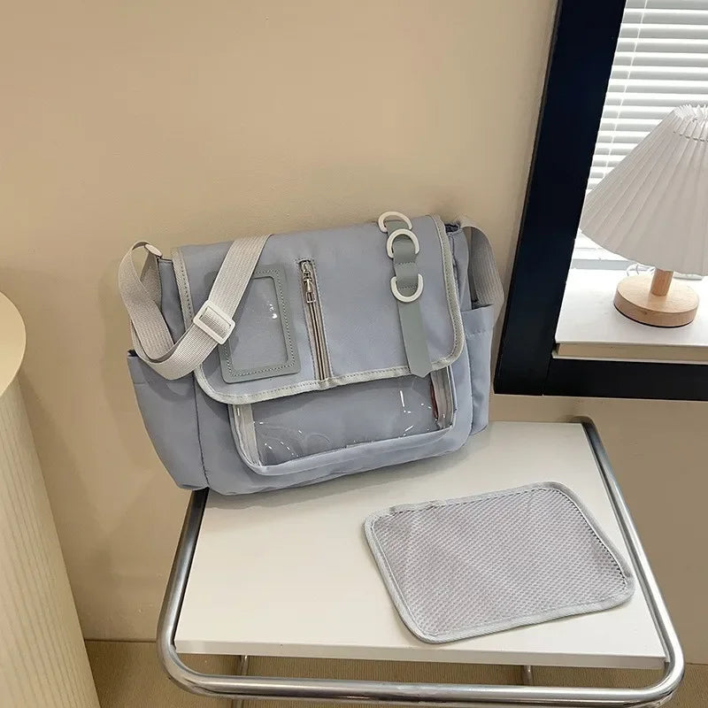 Itabag shoulder bag in light blue-gray with a clear front panel, zippered pocket, and adjustable strap