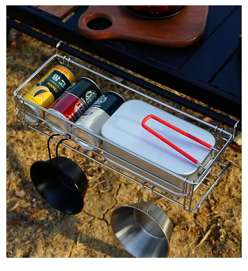 Outdoor aluminum table-side storage rack with hanging mesh basket, holding cans, a white box, and metal cups