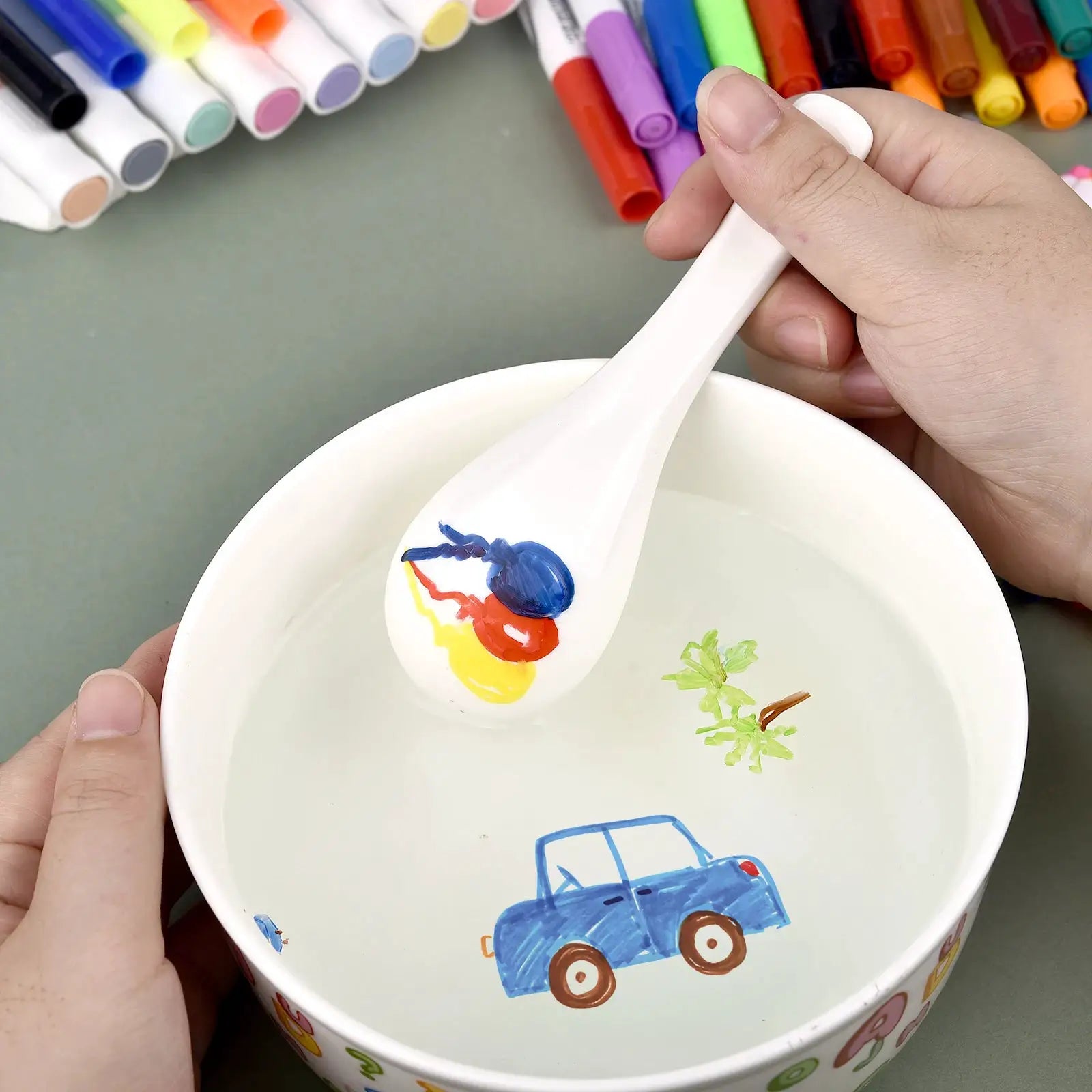 Magical water painting pen set for kids, white spoon with blue paint in a bowl and colorful markers in the background