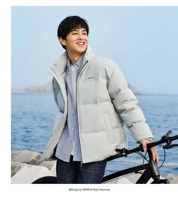 Semir down jacket, light gray puffer outerwear, windproof and waterproof, worn by a man by the sea with a bike.