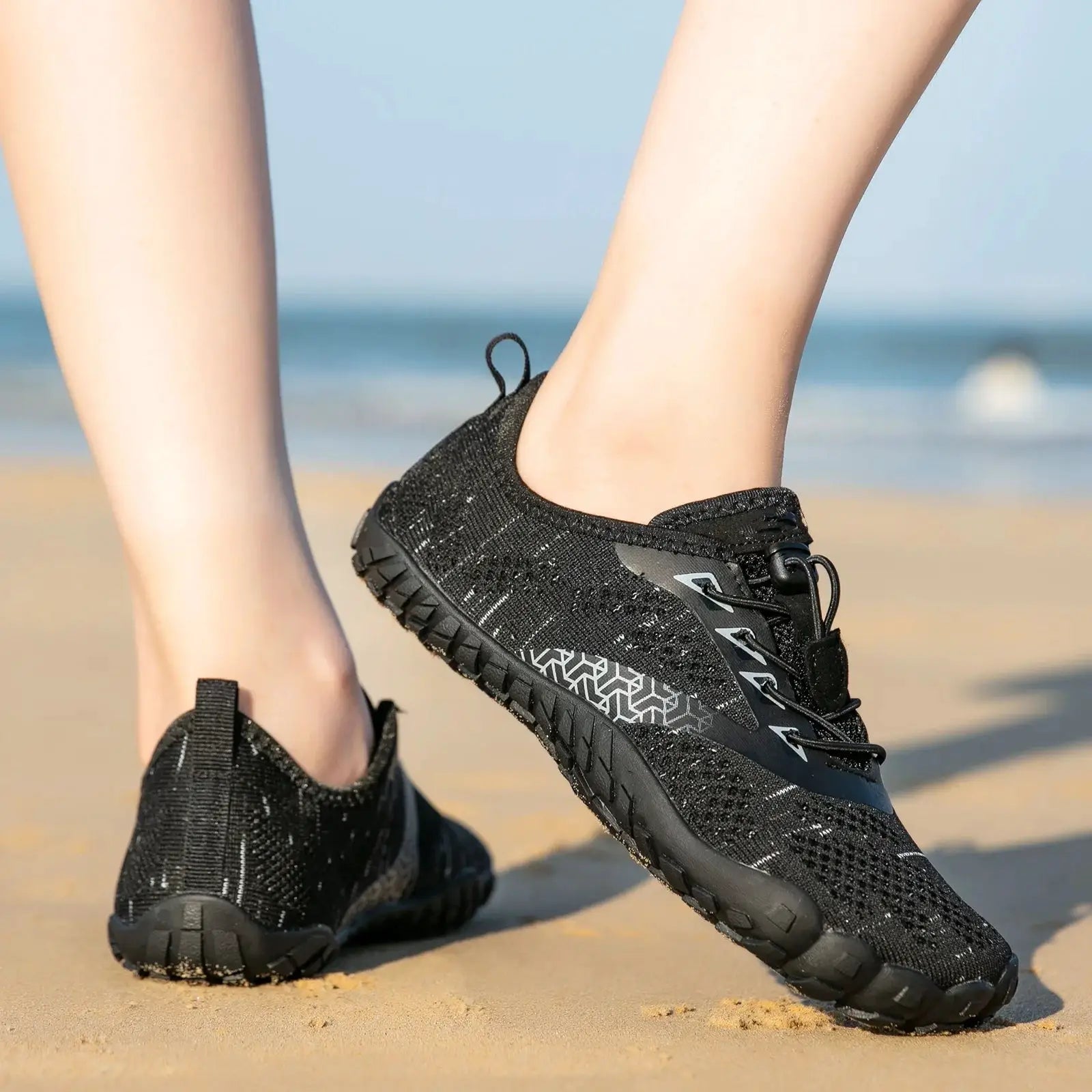 Trail running shoes pair, black knit upper with rugged outsole on sandy beach