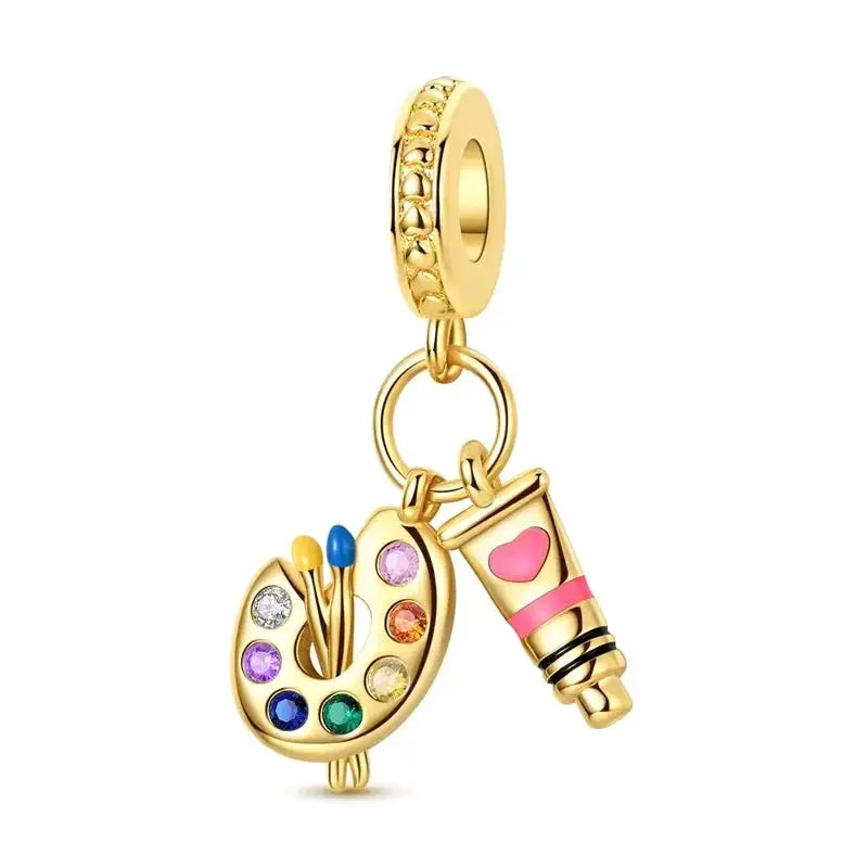 Gold-tone bracelet charm set with a painter palette and lipstick pendants (2 charms)
