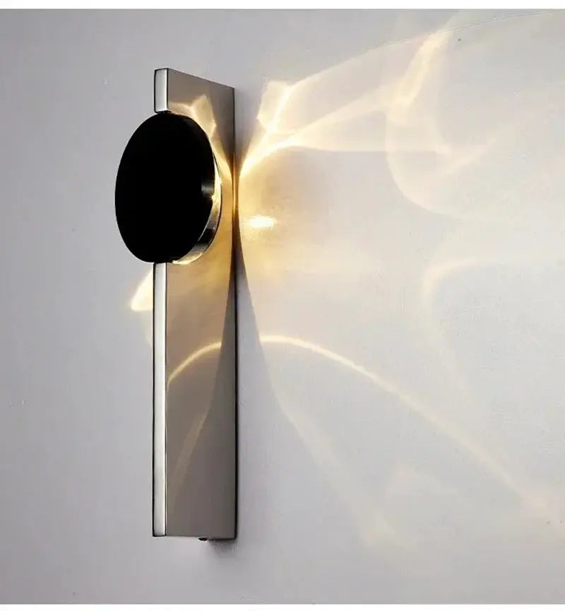 Modern LED wall light with stainless steel backplate and black circular head, wall sconce casting warm glow