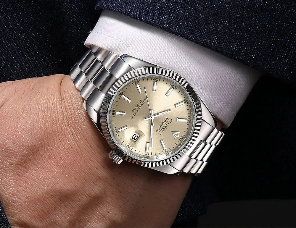 CADISEN men's automatic watch with stainless steel bracelet, champagne dial, date window, and fluted bezel.