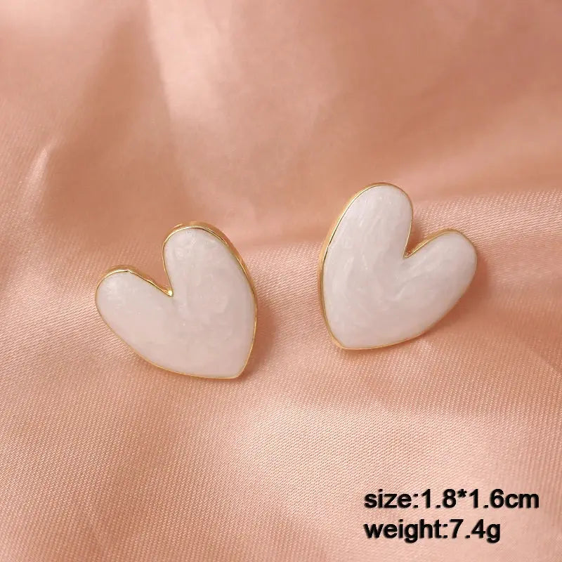 Heart-shaped white enamel earrings with gold trim; pair on pink satin background.