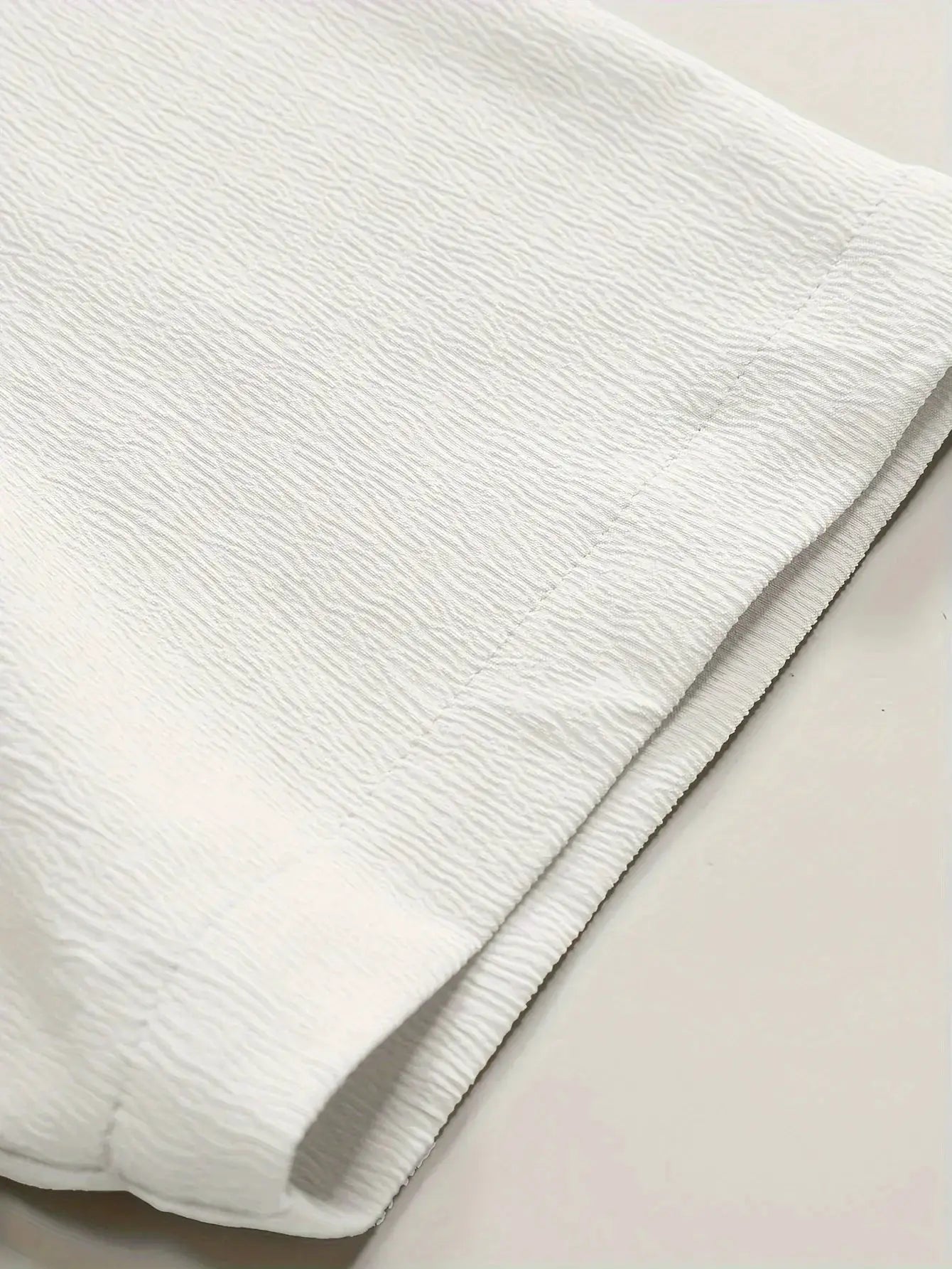 Summer men's short sleeve shirt in solid white linen-textured fabric, folded with visible seam detail