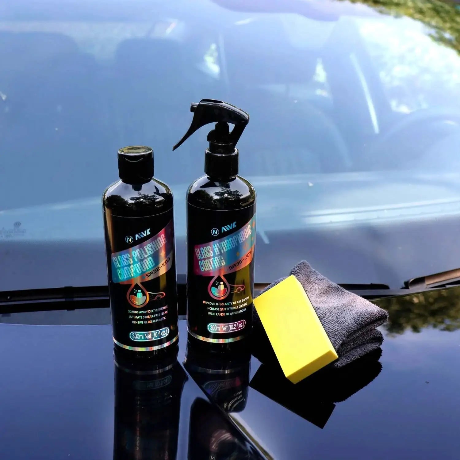 Glass polishing compound bottles with spray bottle on car hood, plus a yellow sponge and microfiber cloth