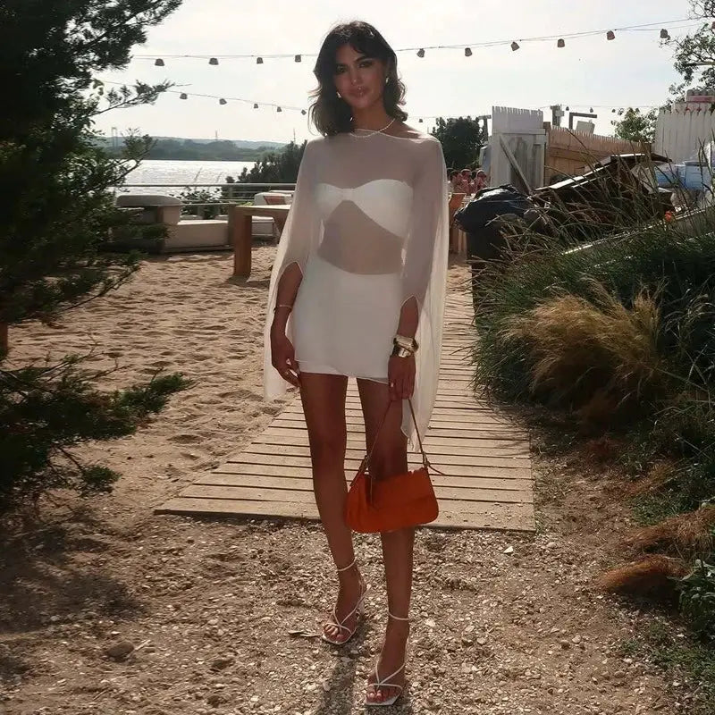 Chiffon see-through blouse with cape overlay, worn over a white dress by a woman at the beach carrying an orange bag.