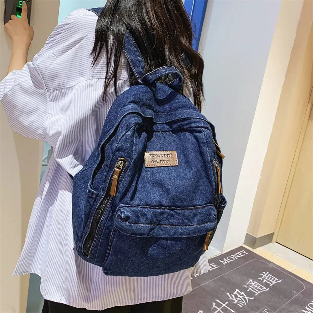 Denim school backpack in dark blue with multiple pockets and gold zippers.