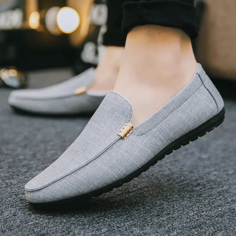 Men's gray canvas slip-on loafers with gold-tone emblem and black sole.