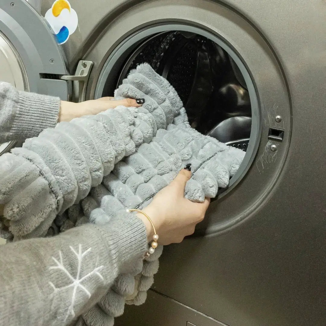 Gray thick-quilted flannel sofa pad being placed into a front-loading washing machine.