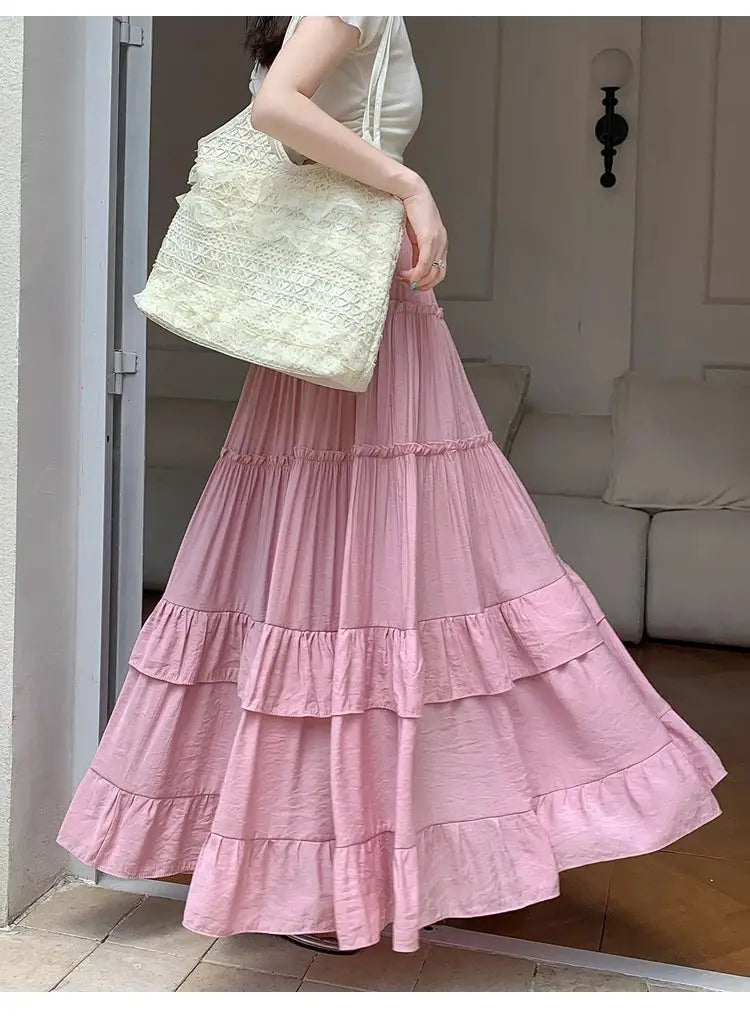Pink tiered maxi skirt with ruffle layers, worn with a cream tote bag.
