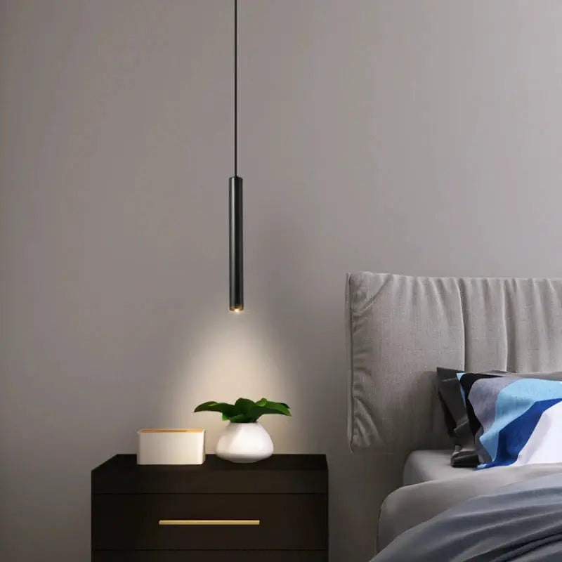 Minimalist bedside pendant lamp by Simples Market, black metal cylinder with warm LED glow over a nightstand.