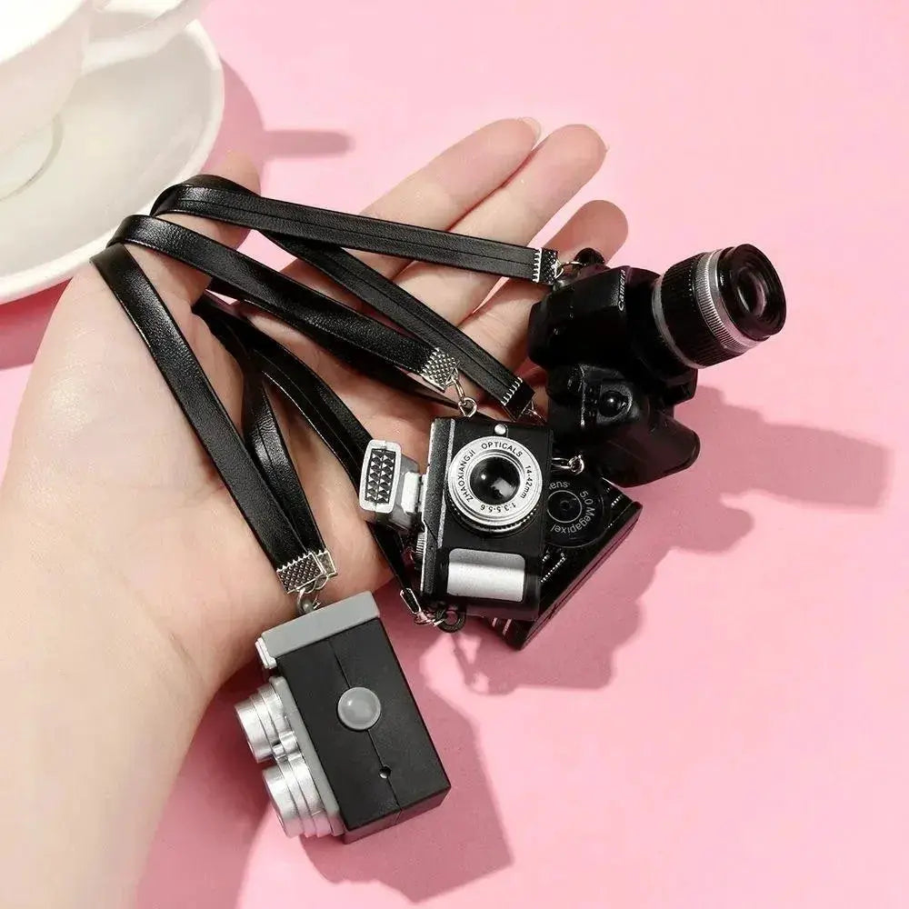Dollhouse miniature digital SLR camera set by Simples Market; four tiny black cameras with silver lenses and straps