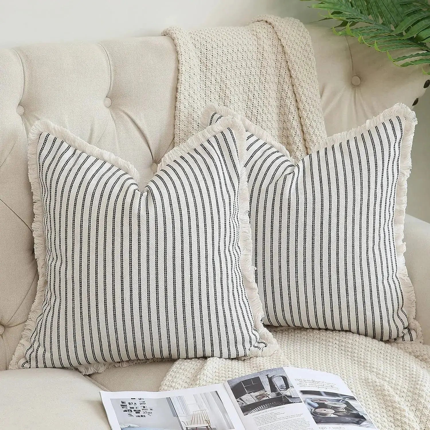 Two wool striped cushion covers with black vertical stripes and fringed edges on a beige sofa