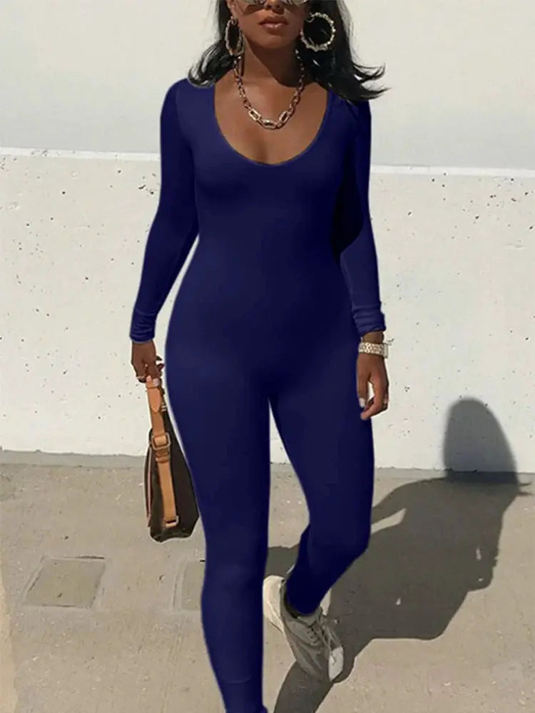 Women's navy blue long-sleeve skinny jumpsuit with scoop neck; paired with white sneakers and brown handbag