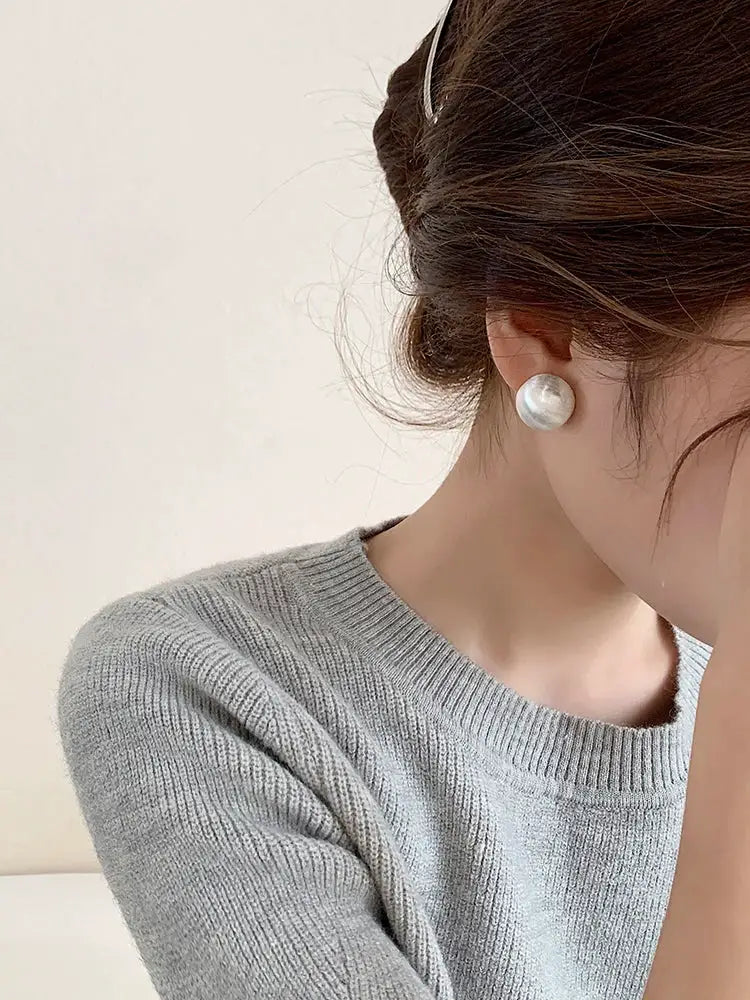 Pearl stud earrings featuring a large white pearl with a glossy finish