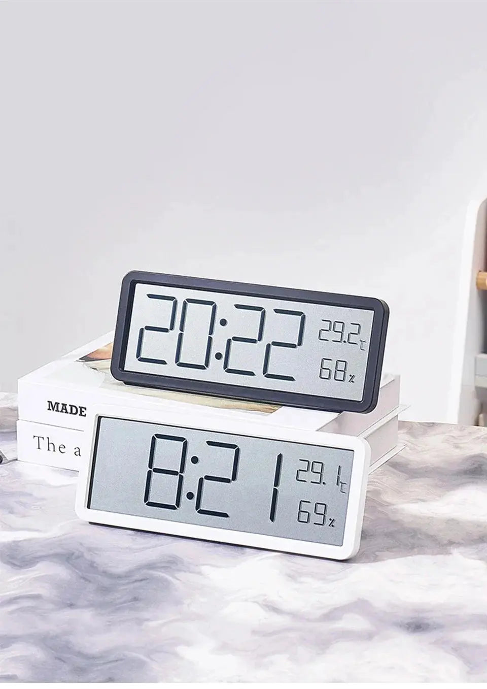Two LCD digital desk clocks with black and white frames displaying time, temperature, and humidity.