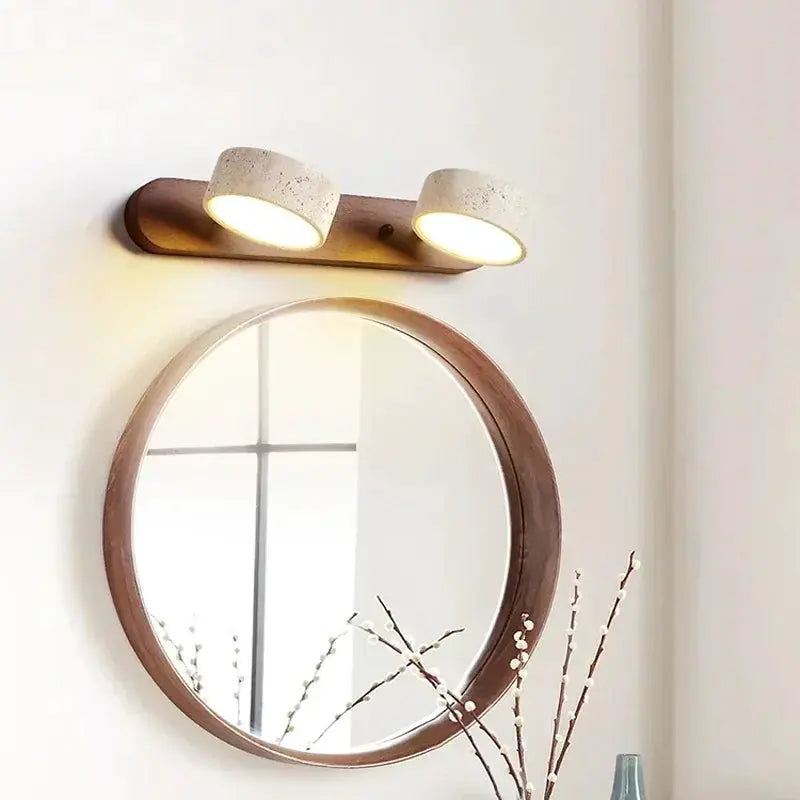 Round wooden-framed mirror with twin concrete-textured LED wall lamps on a wood backplate