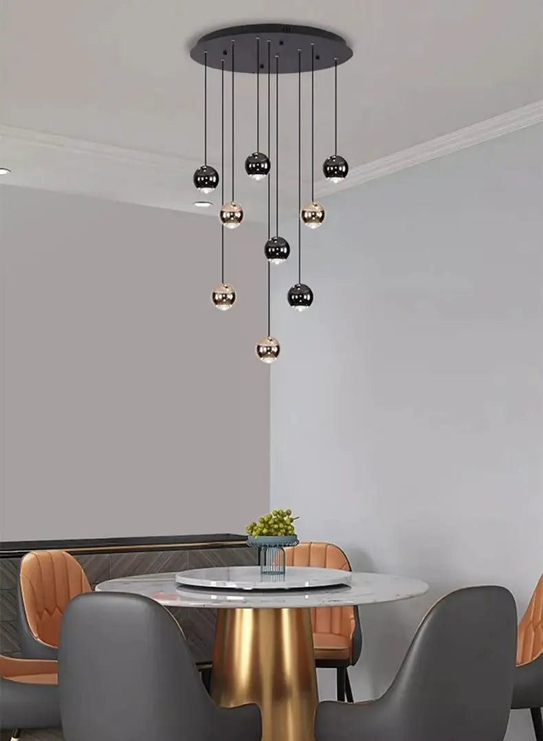 Modern pendant light with multiple black and gold glass globe pendants hanging over a round marble dining table.