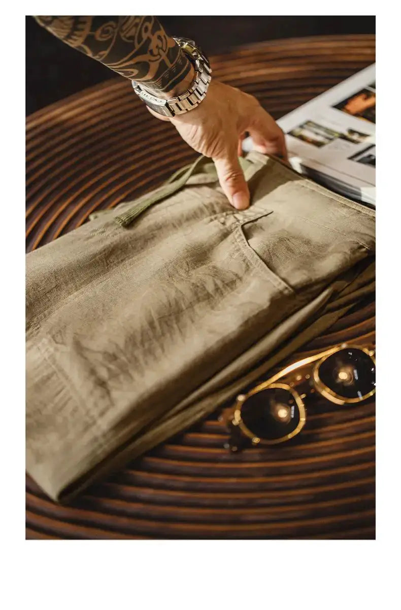 Men's linen-blend khaki chino pants, casual baker style, folded on a wooden table with sunglasses