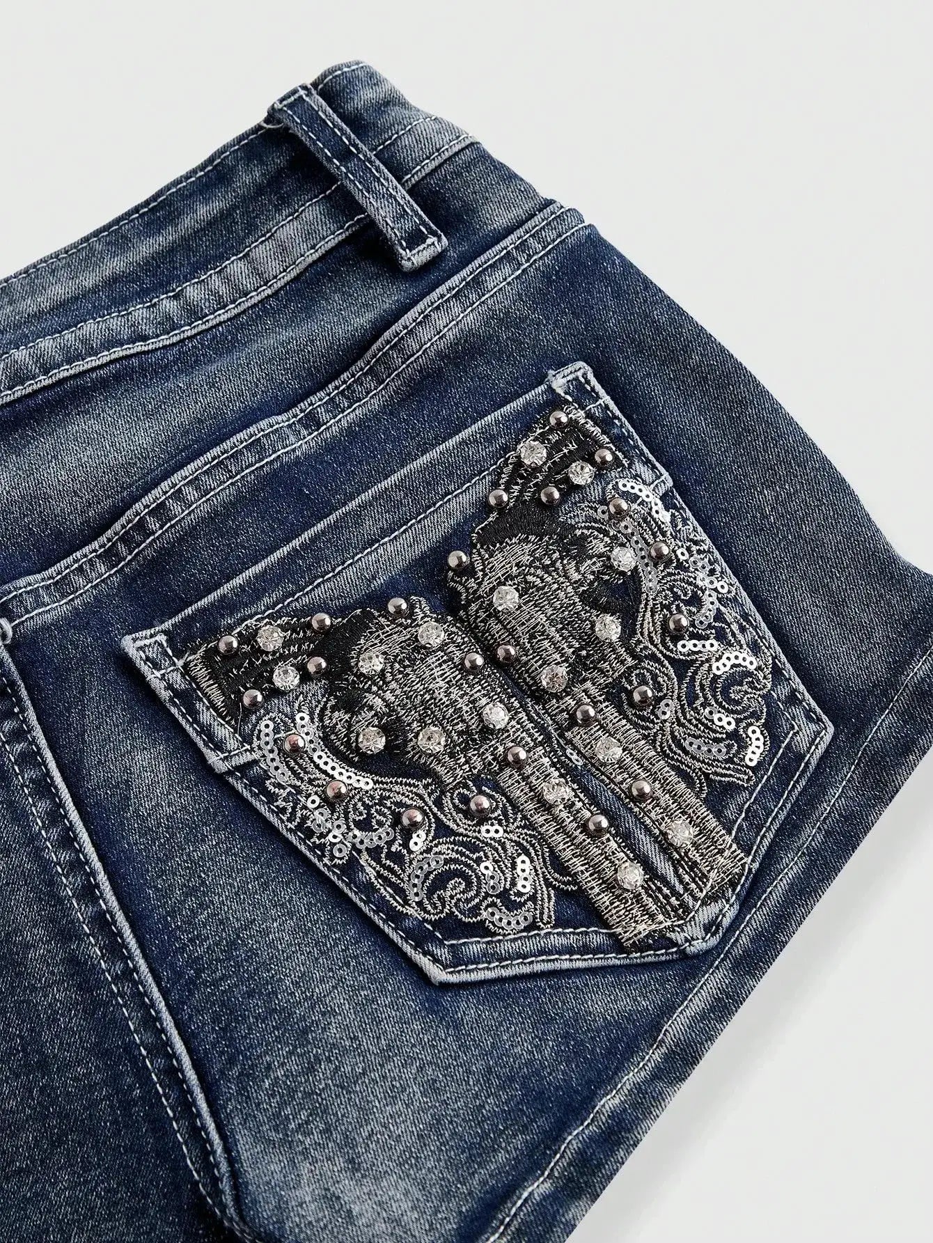 Low rise denim shorts with distressed blue wash and beaded, sequined embroidered back pocket