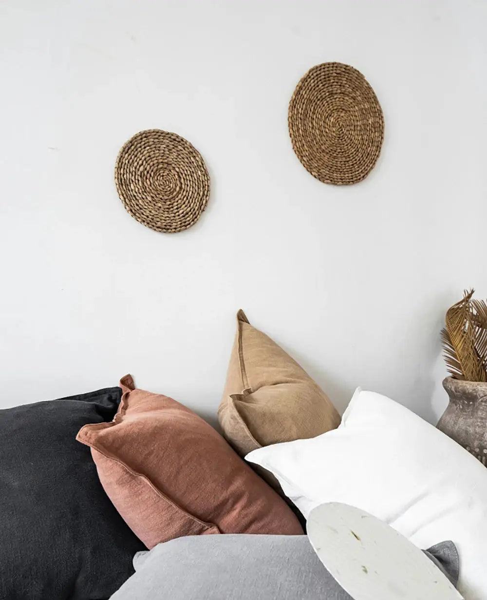 Decorative ramie cushion covers on a sofa with white, gray, rust and beige pillows; two woven wall baskets.