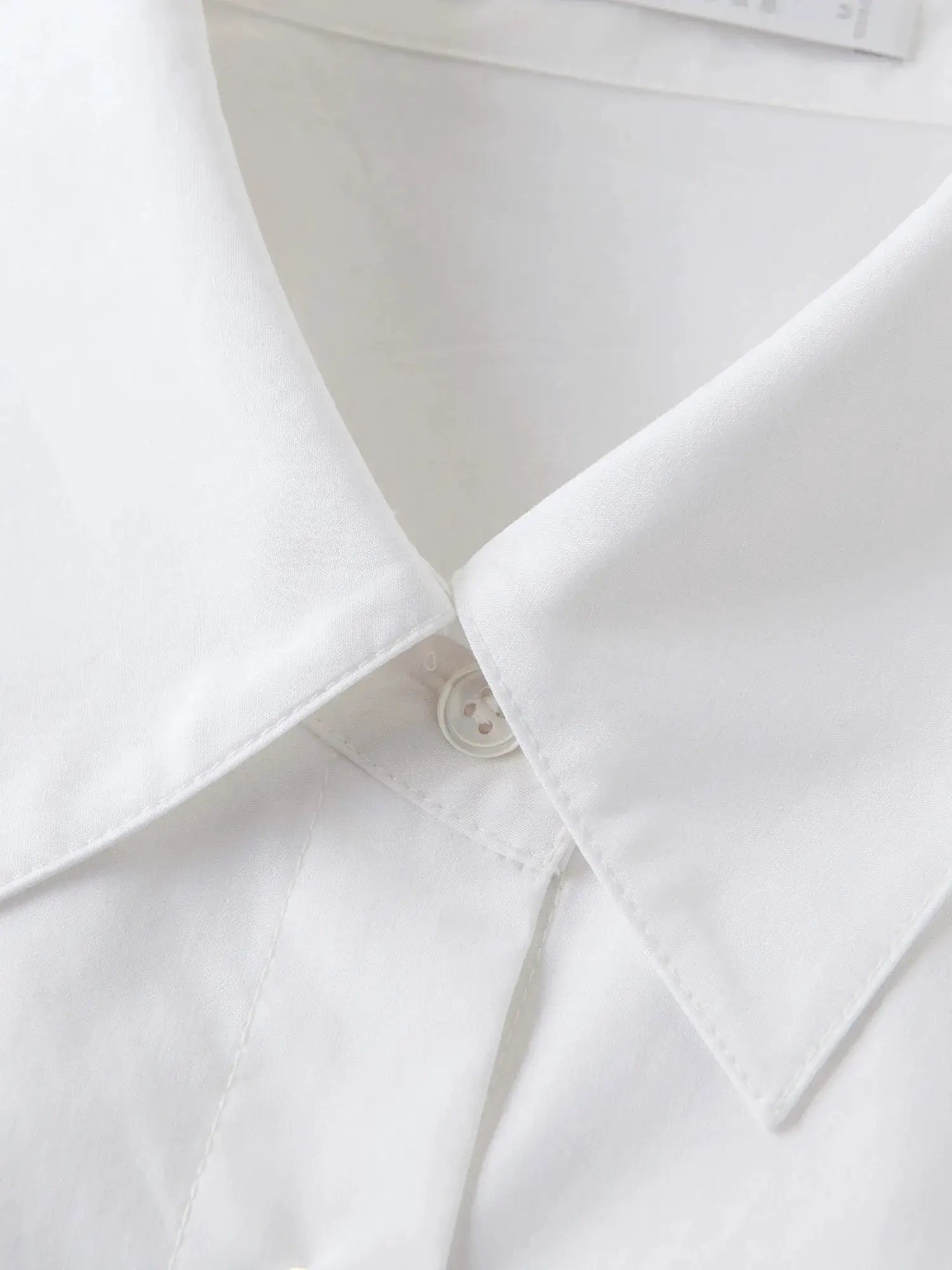 White cotton shirt with collar and button details, close-up of a women's blouse.