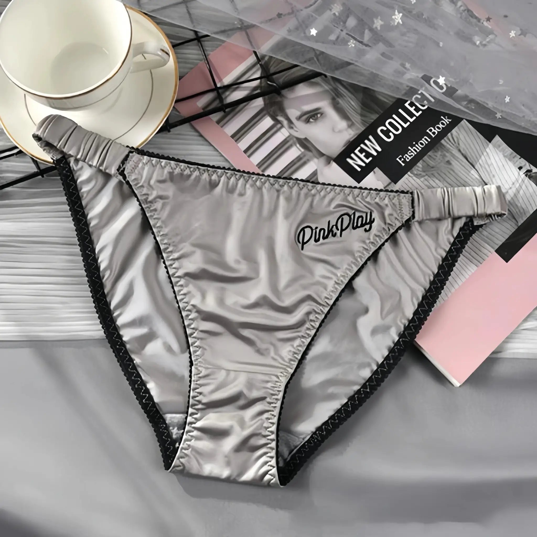 Girls satin panties with black trim and elastic waistband; silver ice silk fabric, several pairs laid out.