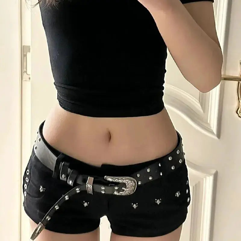 Black low-waist denim shorts with silver studs and a decorative belt, paired with a black crop top.