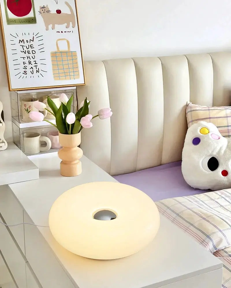 Donut-shaped Bauhaus table lamp in cream on a white bedside table.