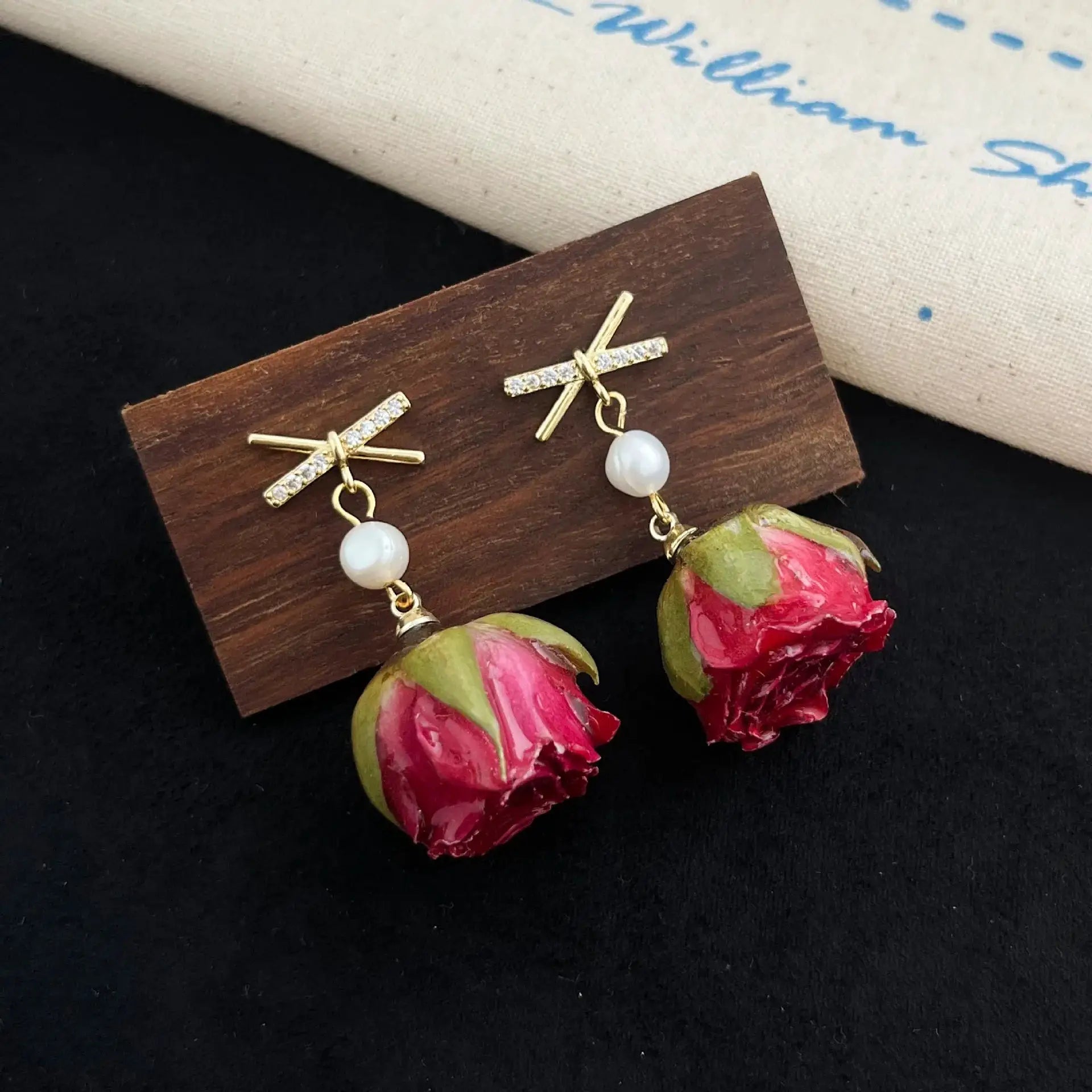 Pair of unique red rose epoxy resin earrings with crystal-studded gold cross accents and dangling pearls
